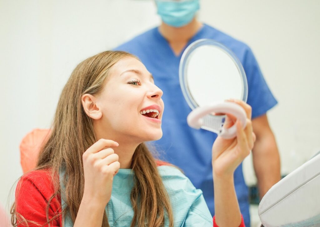 young woman checking their teeth at mirror after dentist